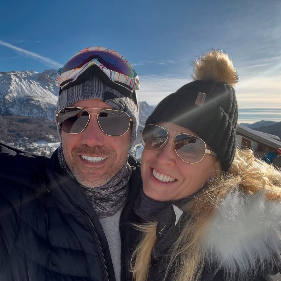 Selfie of a couple in winter clothing, smiling at the camera, in front of a snowy mountain range.