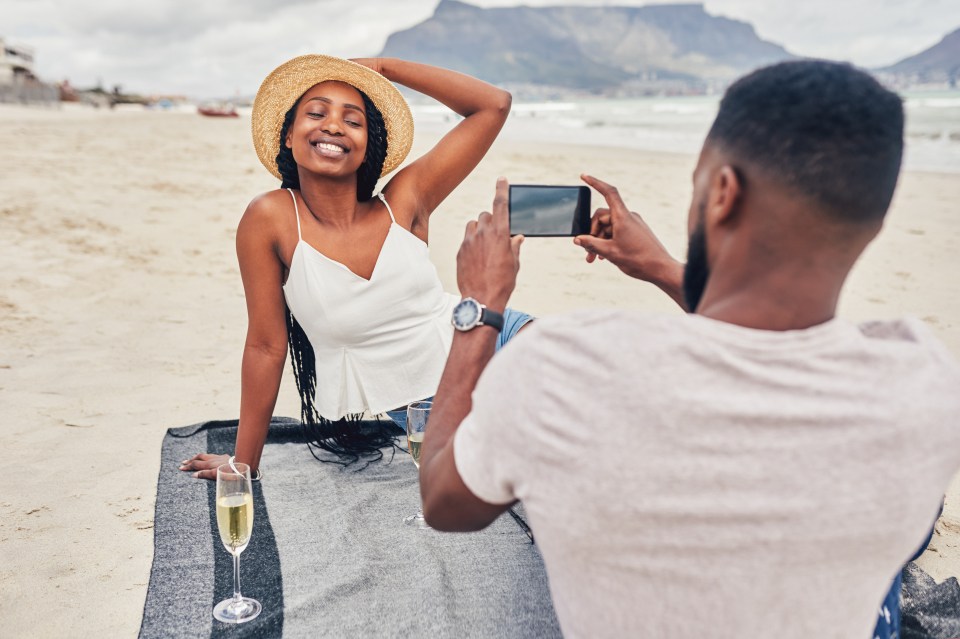 Man taking a photo of his girlfriend on a beach.
