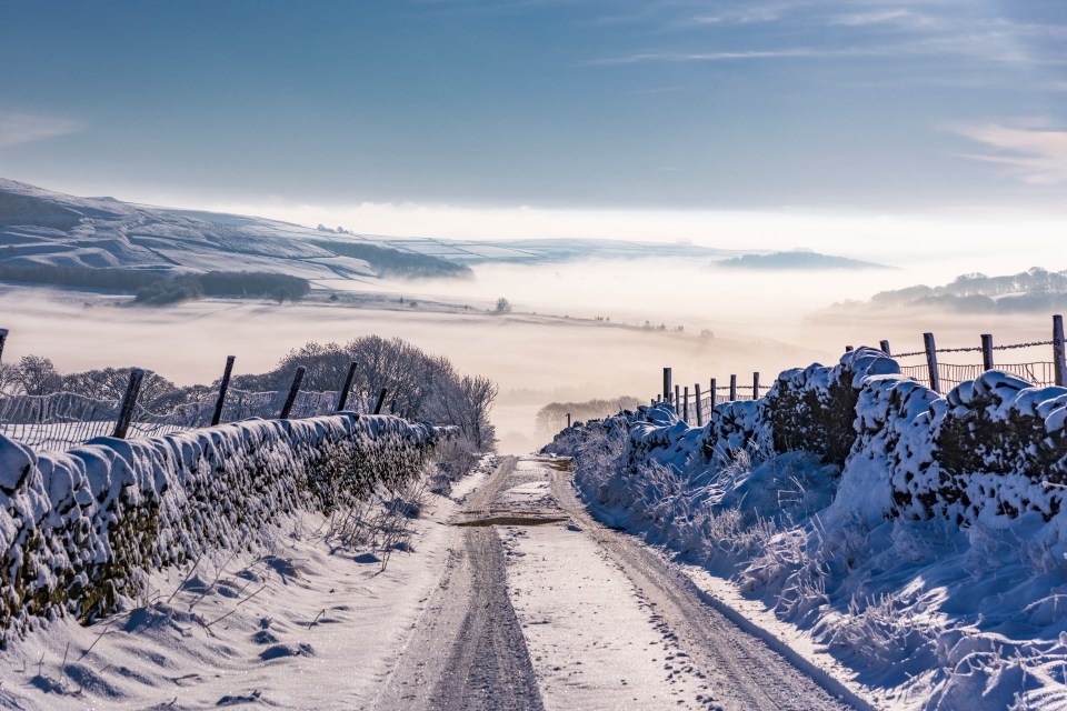 Snow-covered country lane in a misty valley.