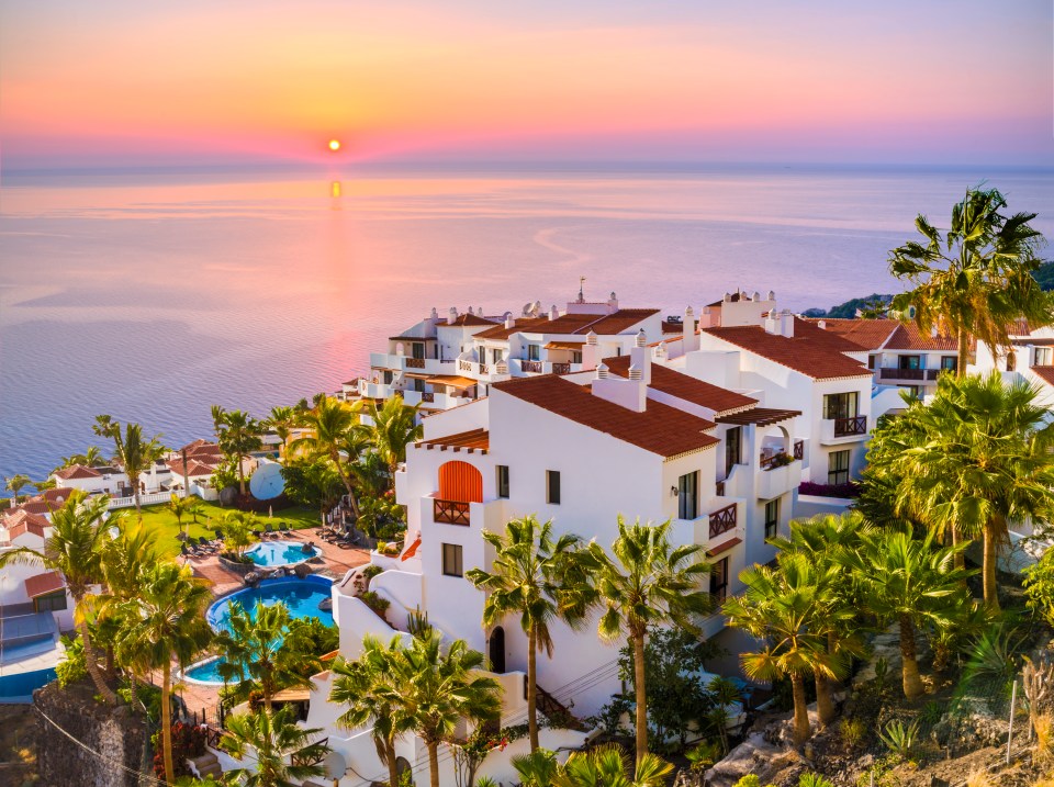 Sunrise over a coastal town with white buildings and palm trees.