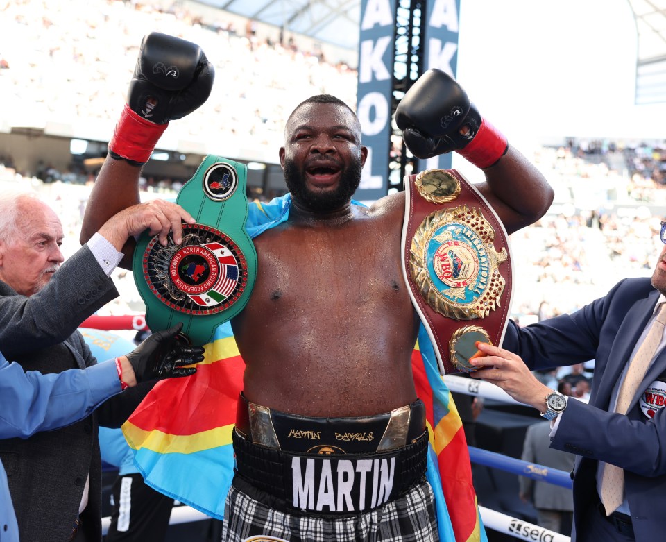 Martin Bakole wins boxing match, holding two championship belts.