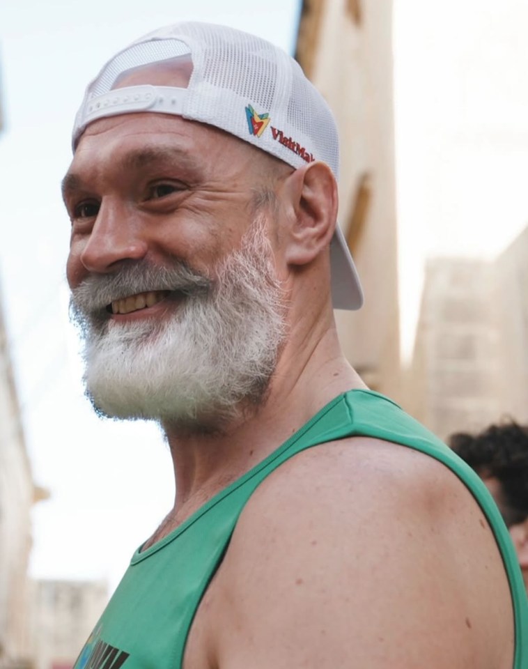 Tyson Fury smiling and wearing a green tank top and white cap.