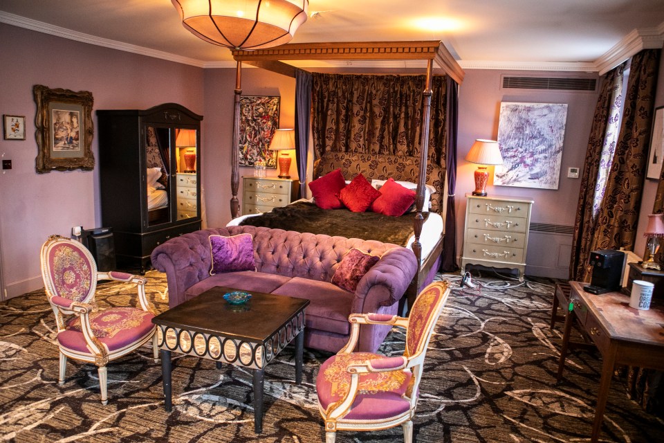 A lavish bedroom with a four-poster bed, purple sofa, and ornate chairs.