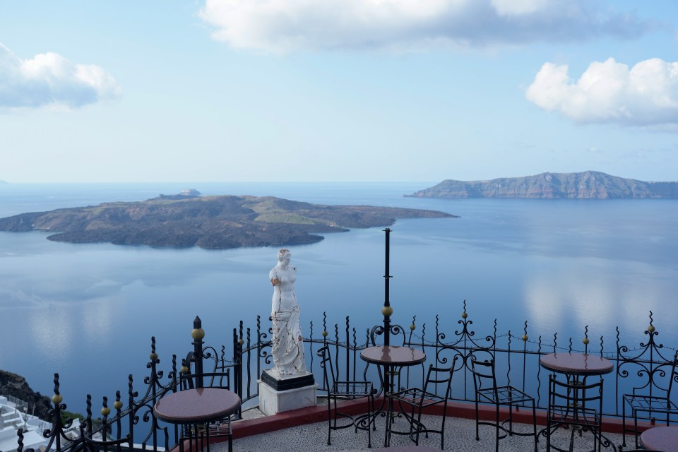 Nea Kameni volcanic island viewed from Santorini, Greece, with outdoor seating and a statue.