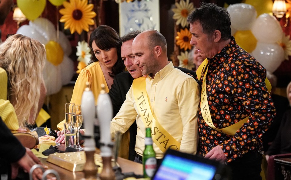 A group of people at a stag do looking at a small cake.