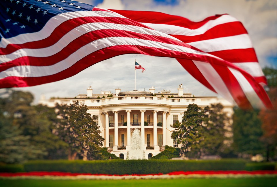 The White House with a waving American flag in the foreground.