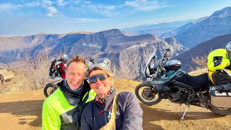 Selfie of a couple on motorcycles overlooking a mountain range.