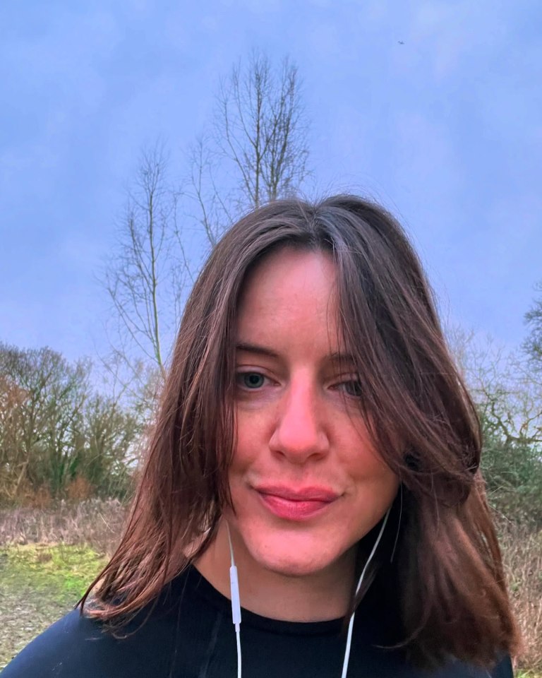 Woman with long brown hair and earphones outdoors.