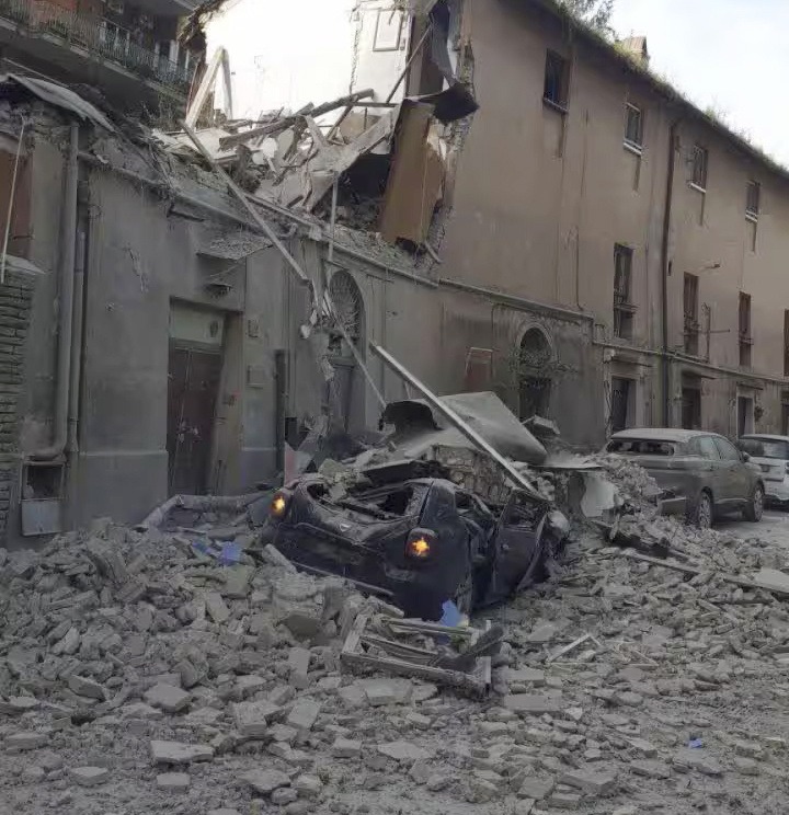 Debris and a damaged car in front of a collapsed building.