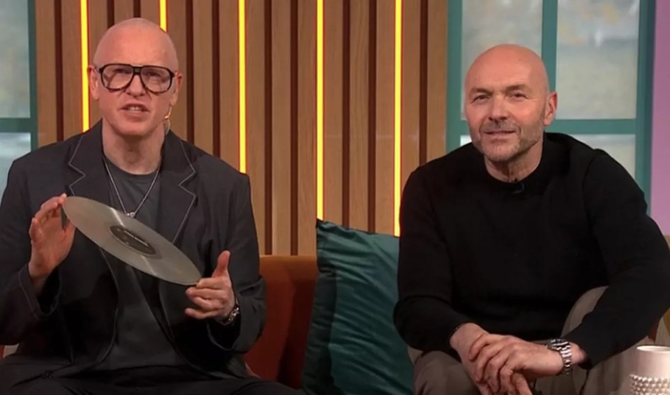 Two bald men sitting on a couch, one holding a silver record.