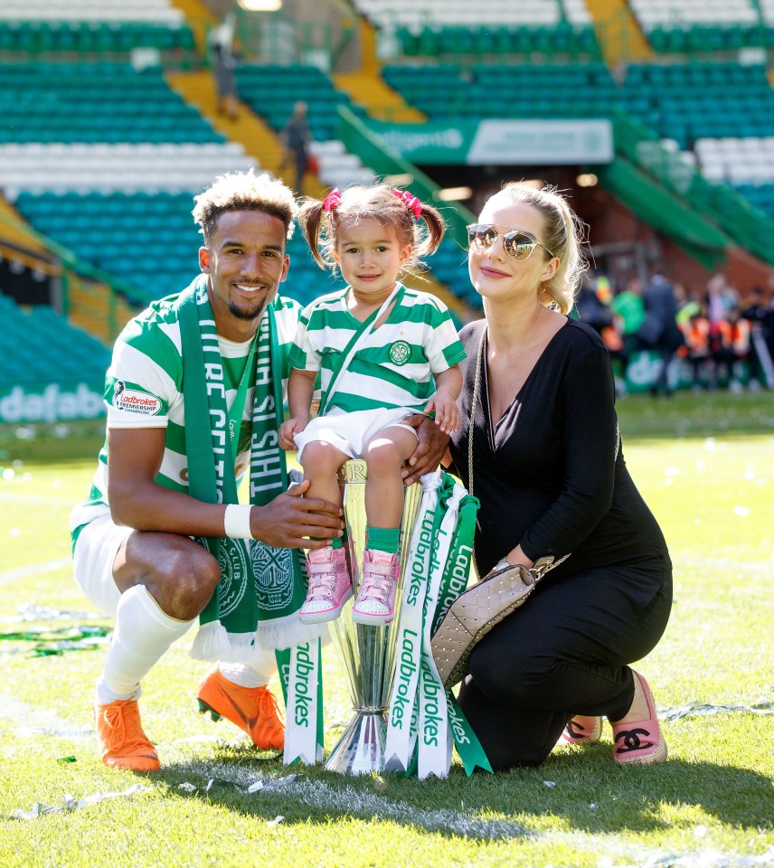 A soccer player, his daughter, and his partner posing with a trophy.