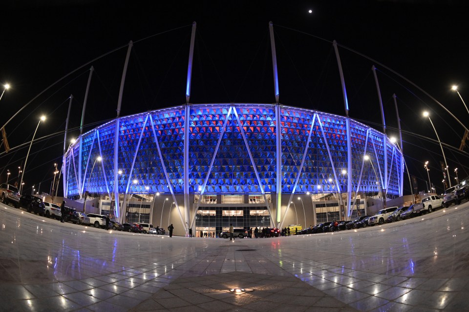 Exterior view of a stadium at night, illuminated in blue and red.