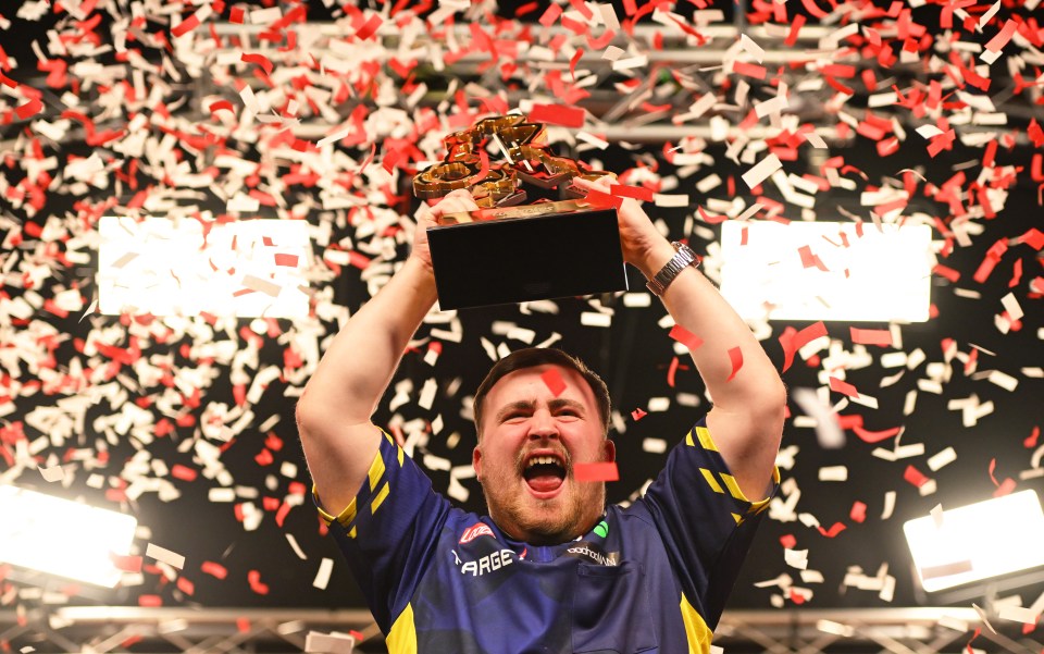 Luke Littler holding up the Ladbrokes UK Open Trophy amidst confetti.