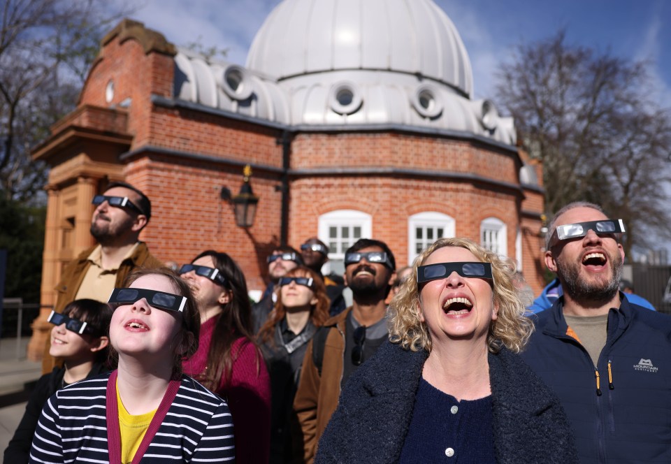 People wearing eclipse glasses watch a partial solar eclipse at an observatory.