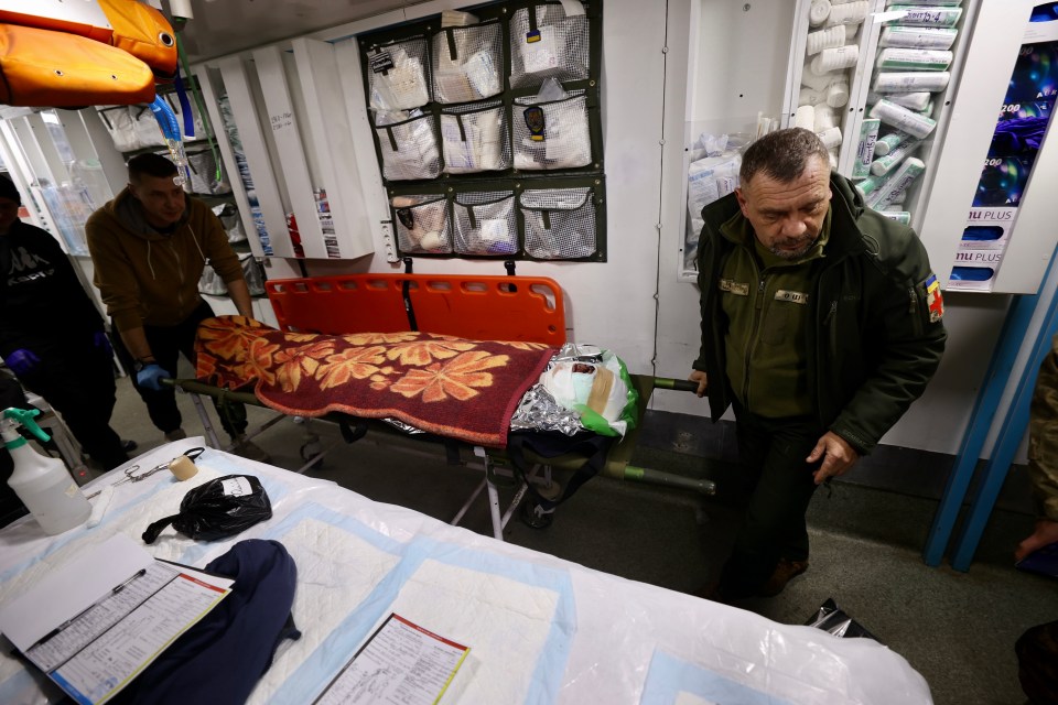 Medics moving a wounded soldier on a stretcher in a mobile field hospital.