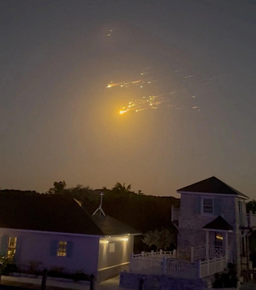 Debris streaking across the night sky over houses.