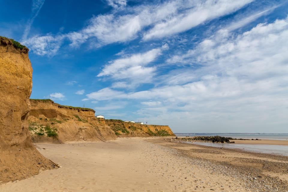Sandy beach with eroding cliffs and a partly cloudy sky.
