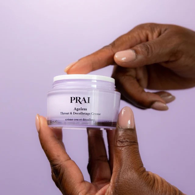 Hands holding a jar of PRAI Ageless Throat & Decolletage Creme.