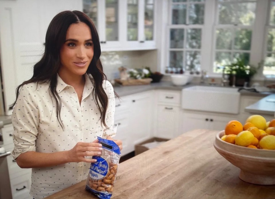 Meghan Markle holding a bag of pretzels in a kitchen.
