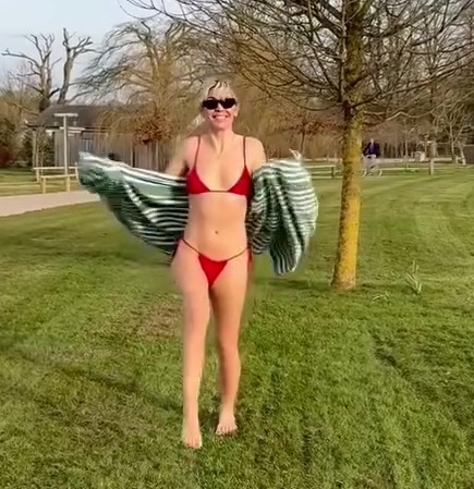 Woman in red bikini walking across a grassy field.