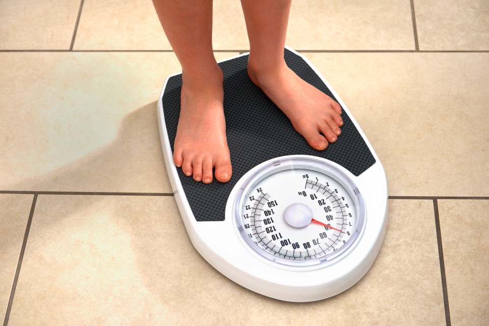 A barefoot boy weighing himself on a bathroom scale.