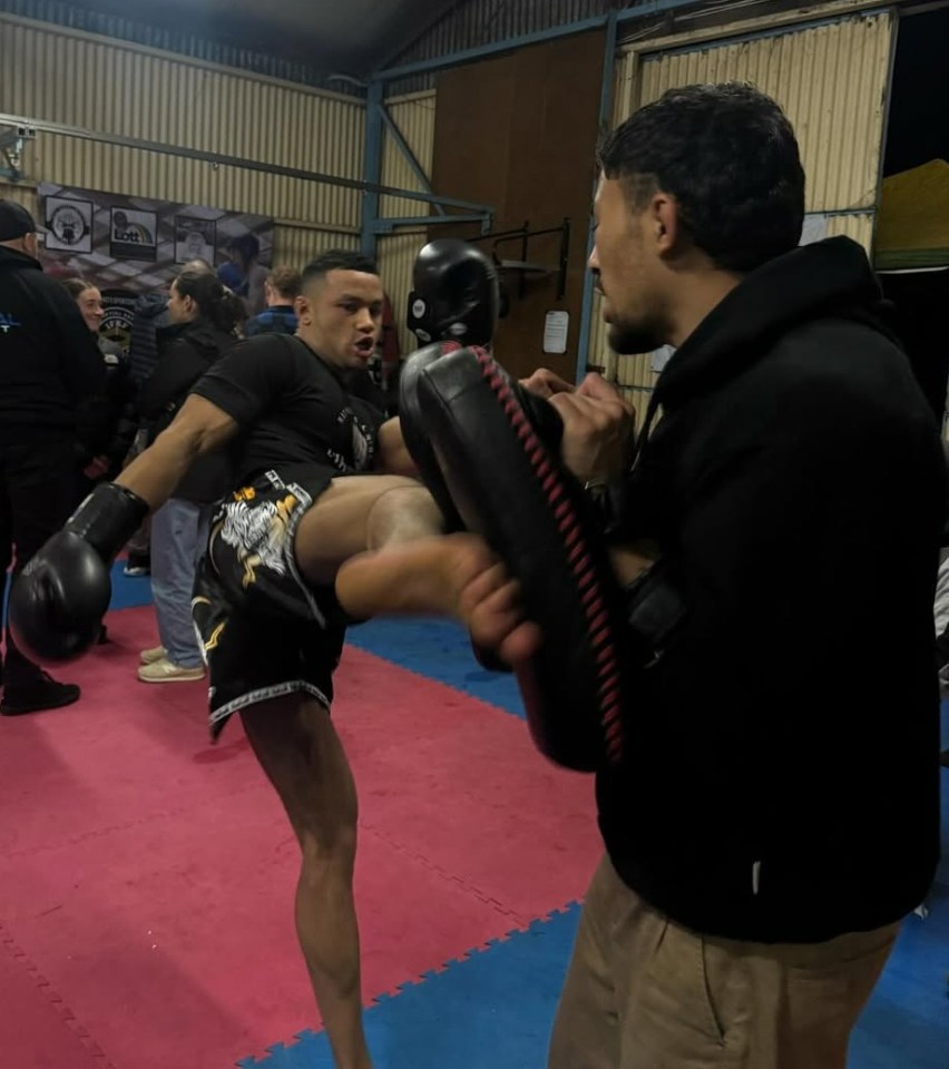 A Muay Thai fighter kicking pads held by a trainer.