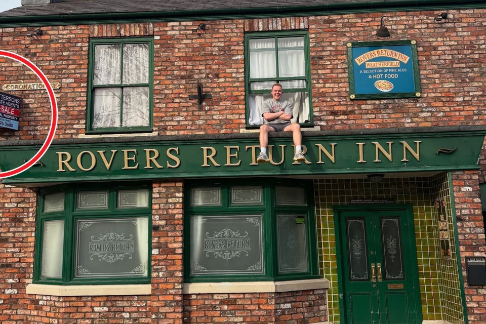 Man sitting on the Rovers Return Inn sign.