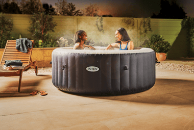 Two women relaxing in an Intex hot tub at night.
