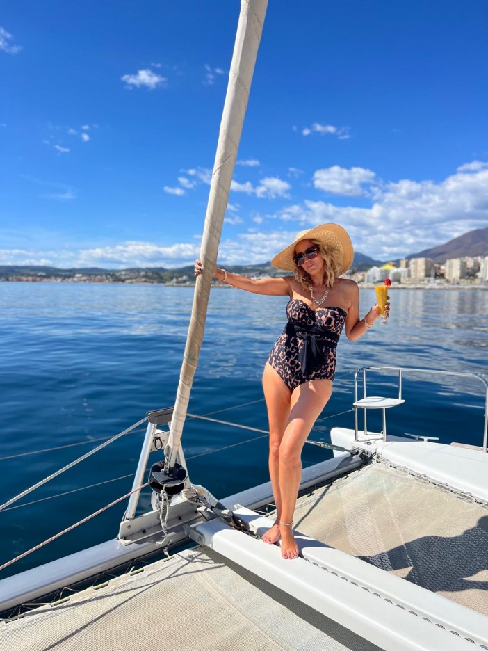 Woman in a swimsuit and hat on a sailboat, holding a cocktail.