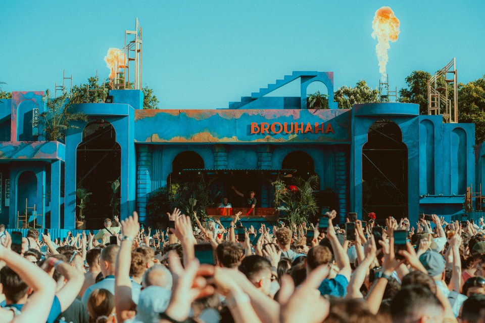 Crowd at a music festival in front of a blue stage with fire effects.