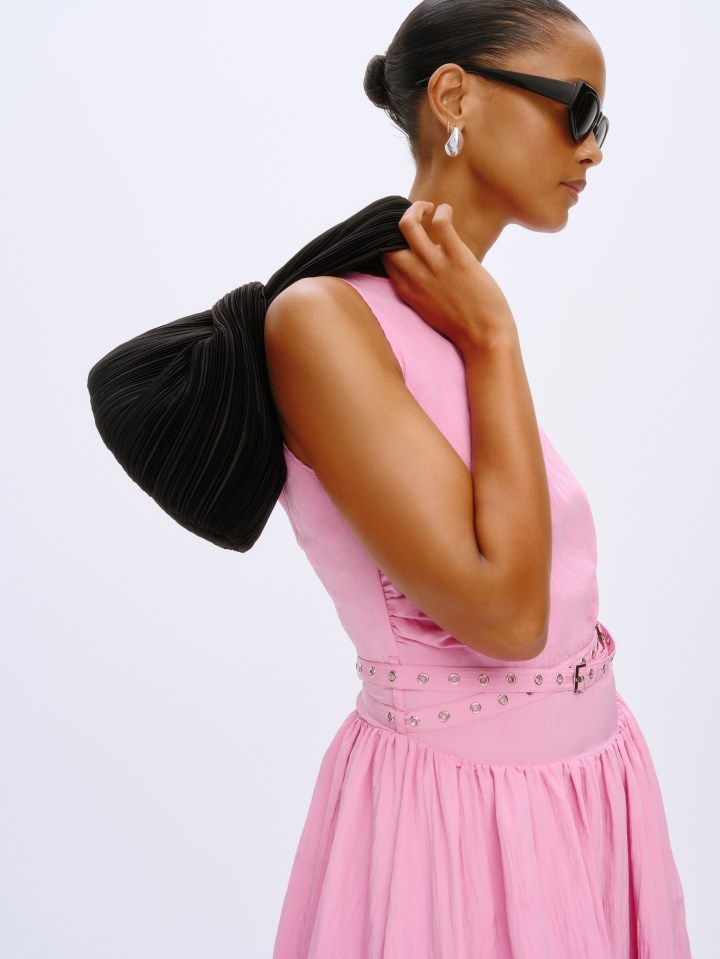 Woman in pink dress and black pleated bag.
