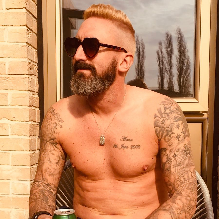 Shirtless man with tattoos and heart-shaped sunglasses.