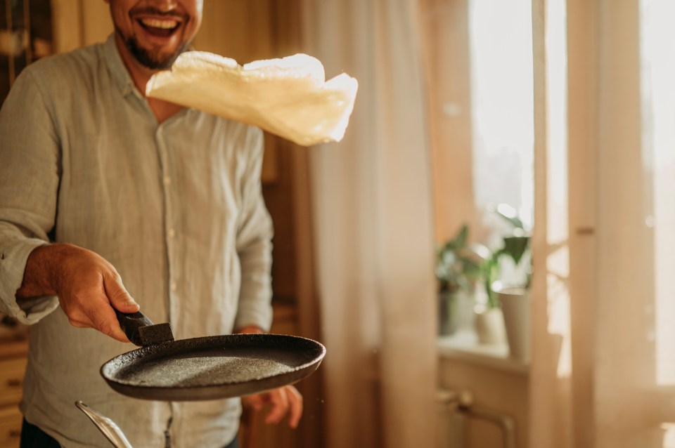 Man flipping a pancake in a frying pan.