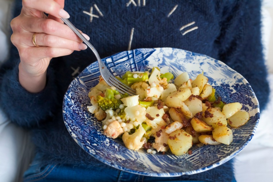 Woman eating a plate of roasted potatoes, cauliflower, broccoli, and couscous.