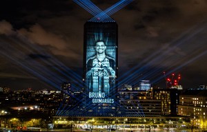 Image of a building at night with a projection of Bruno Guimarães on its facade.