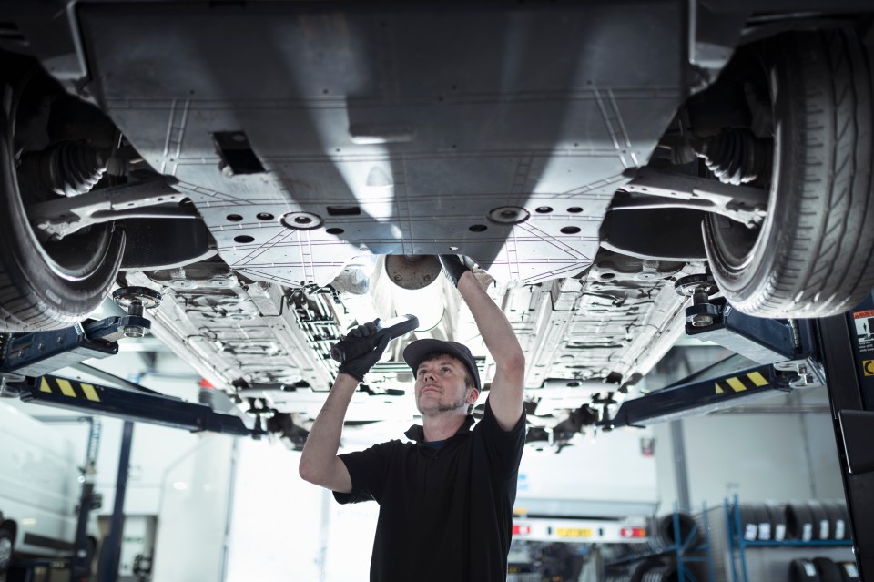 A mechanic examines the underside of a car on a lift.