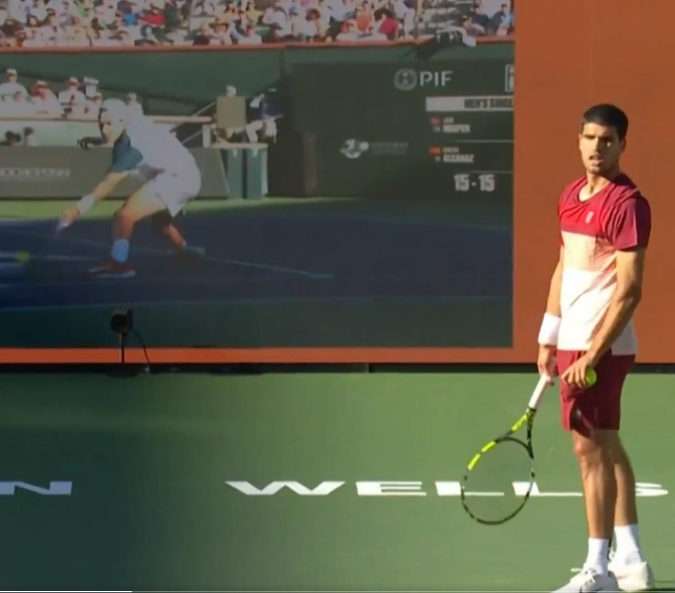 Tennis player on court with jumbotron showing tennis match.