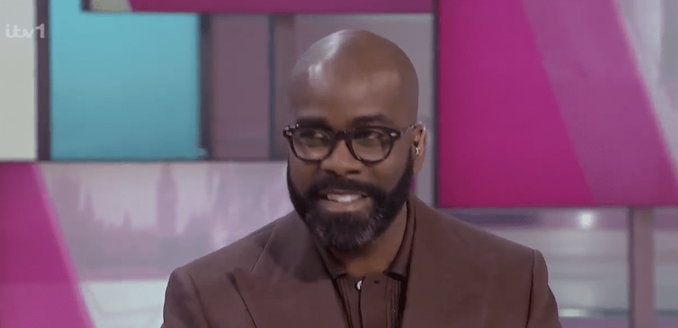 Man in brown jacket and glasses smiling.