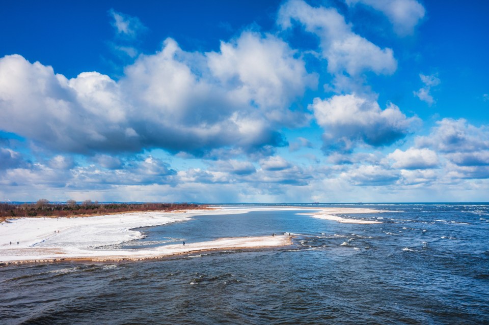 Snowy beach and ocean under a cloudy sky.
