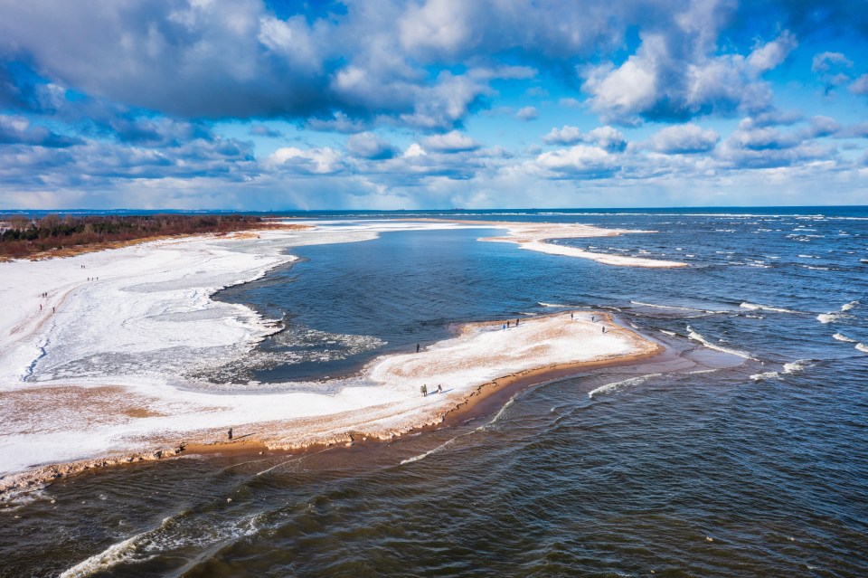 Aerial view of a snow-covered beach and partially frozen ocean.