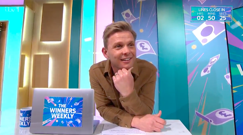 Screenshot of a man sitting at a desk, smiling; a laptop with "The Winners Weekly" logo is visible.  A timer shows 2 hours, 50 minutes, and 25 seconds remaining.