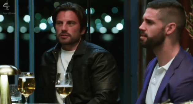 Screenshot of two men sitting at a table, drinking beer.