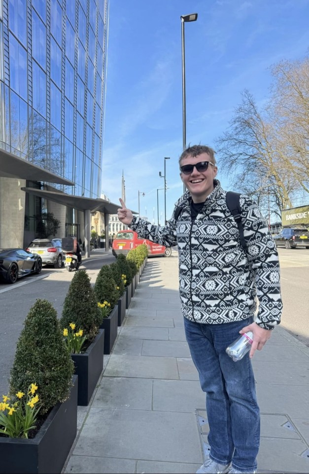 Man pointing, standing on a city street with daffodils and a luxury car.