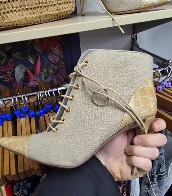 Person holding up a beige lace-up shoe with a crocodile-embossed heel.