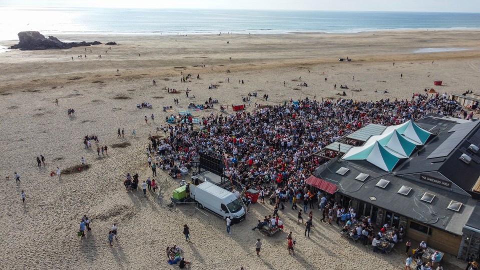 Aerial view of thousands of England football fans on a beach watching a match.