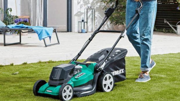 Person using a teal and black lawnmower on a lawn.
