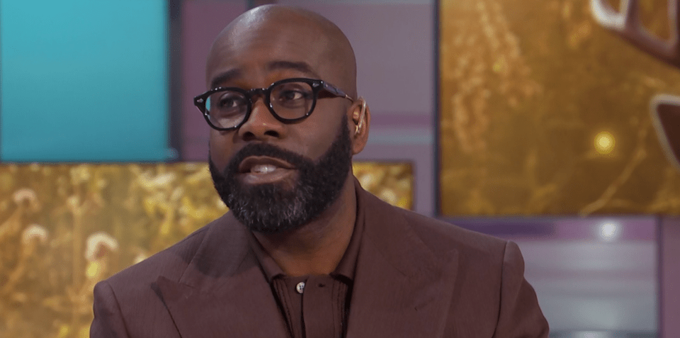 Man in brown jacket and glasses being interviewed.