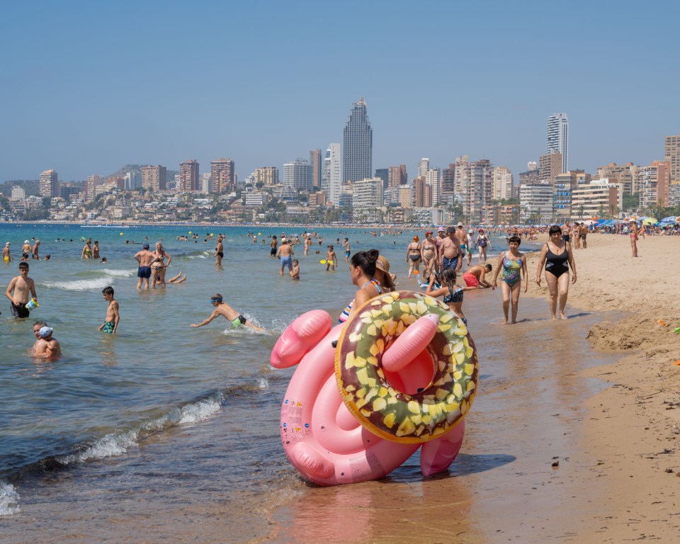 Crowded Benidorm beach with a woman holding a flamingo-shaped inflatable ring.