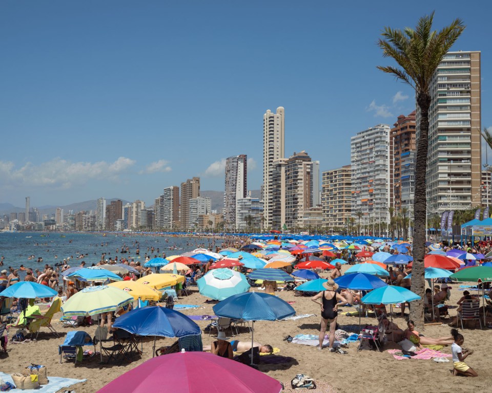 Crowded Benidorm beach with colorful umbrellas and high-rise buildings in the background.