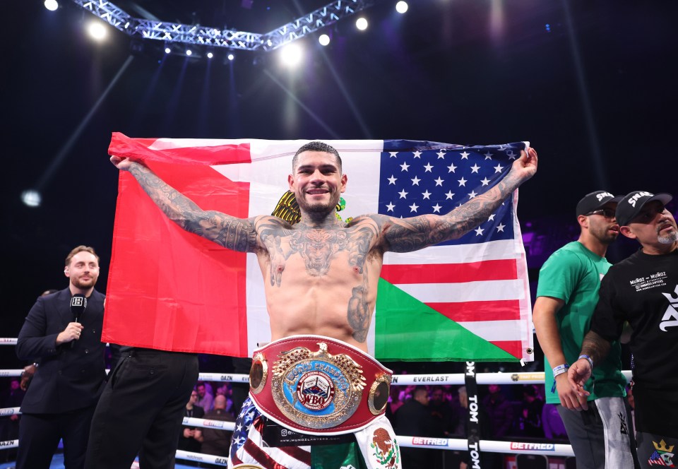 Boxer Arnold Barboza Jr. holding championship belt and flags after a boxing match win.